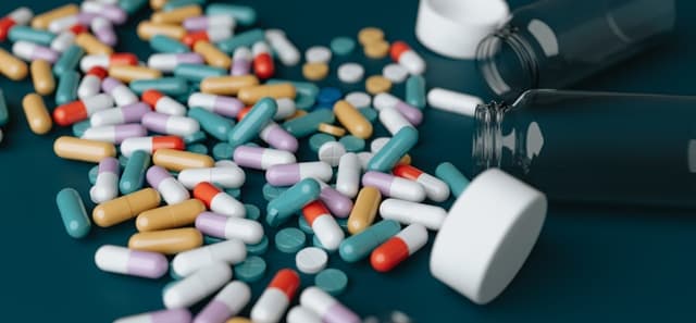 A variety of pills and capsules scattered across a wooden table surface, showcasing different shapes and colors.