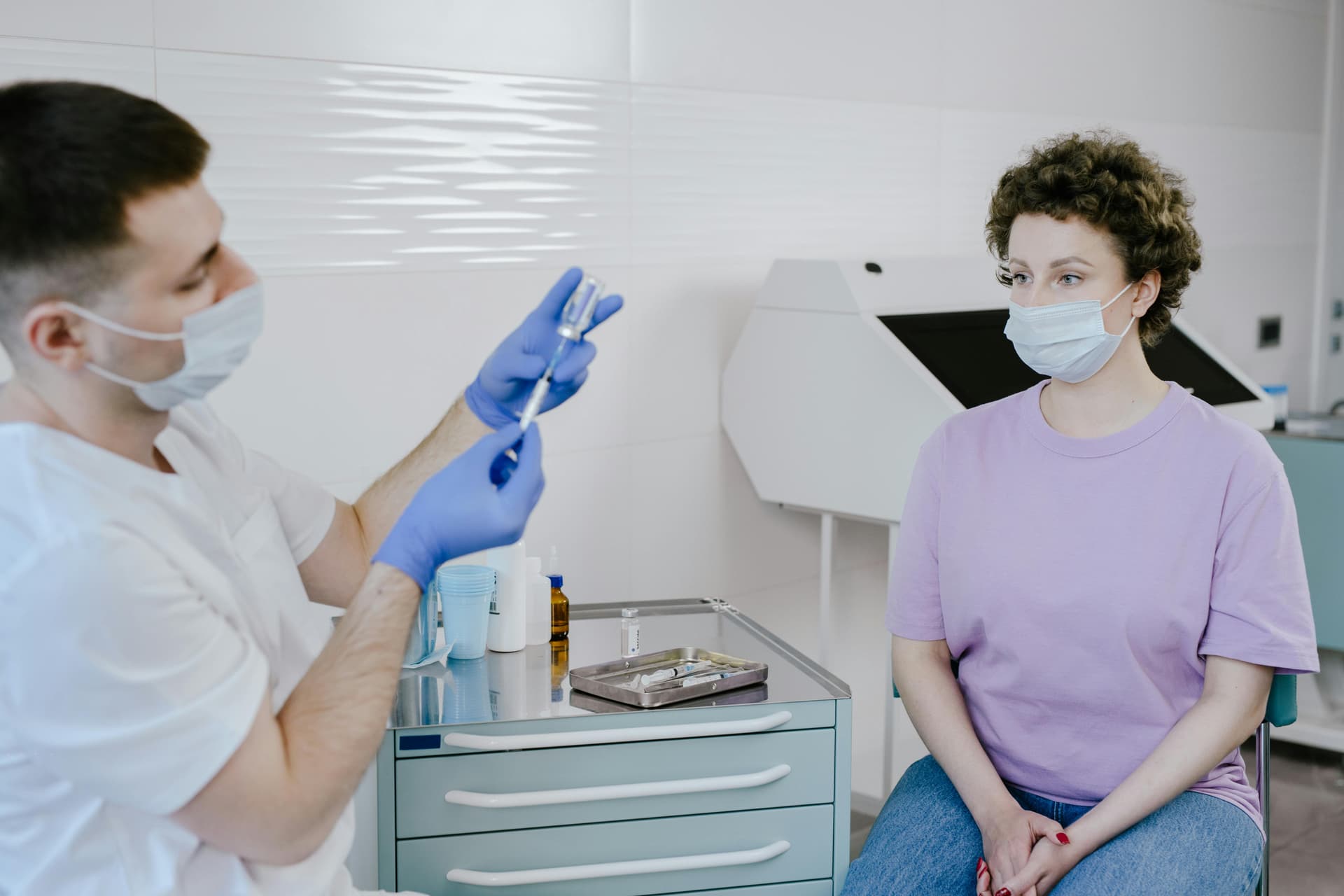 A woman in a hospital gown receives a checkup from a doctor in a clinical setting.